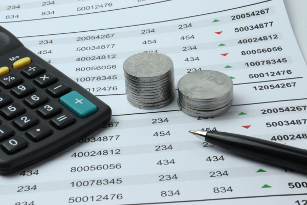 Calculator and coins placed on top of a sheet with figures that go into company presentation design.