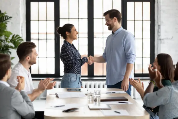 HR manager shakes hands with new hire during employee onboarding.